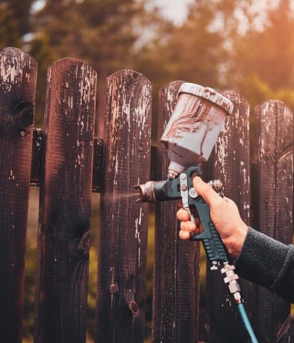 A person spraying paint on a wooden fence.